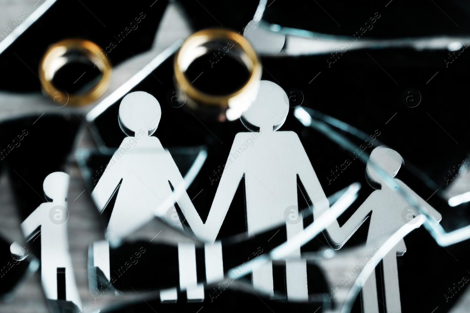 Photo of Divorce concept. Human figures reflected in broken mirror and wedding rings on table, closeup