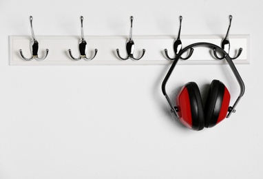 Photo of Protective headphones hanging on white wall. Safety equipment