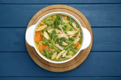Photo of Saucepan of delicious vegetable soup with chicken on blue wooden table, top view