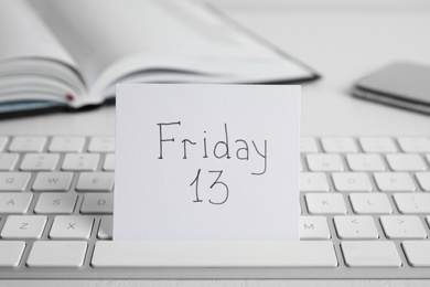 Photo of Paper note with phrase Friday 13 and keyboard on white table. Superstition of bad luck