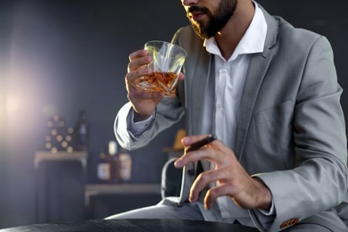 Photo of Man with glass of whiskey and cigar sitting at table, closeup. Space for text