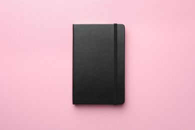 Photo of Closed black notebook on light pink background, top view