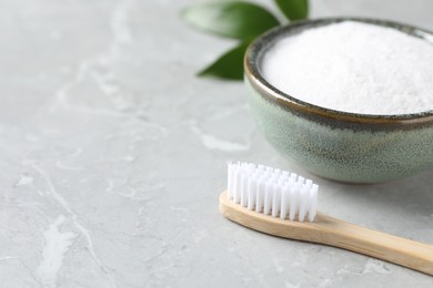 Bamboo toothbrush and bowl of baking soda on light gray marble table, closeup. Space for text