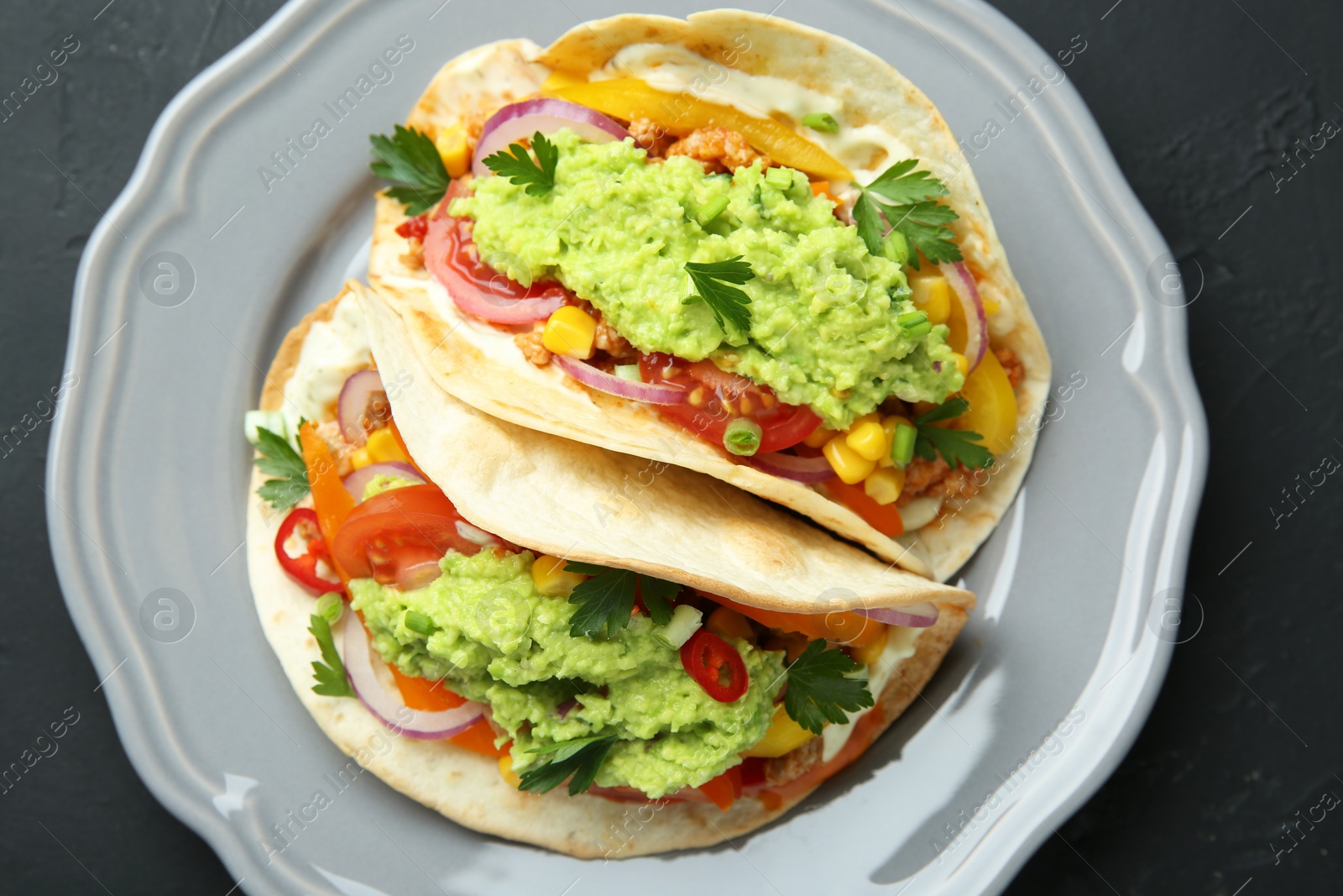 Photo of Delicious tacos with guacamole, meat and vegetables on black table, top view