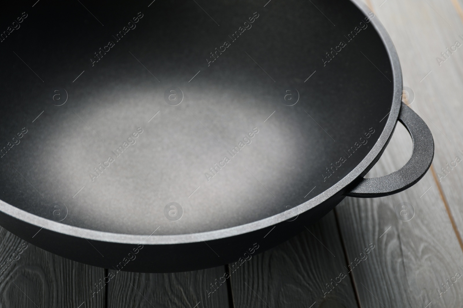 Photo of Empty iron wok on grey wooden table, closeup. Chinese cookware