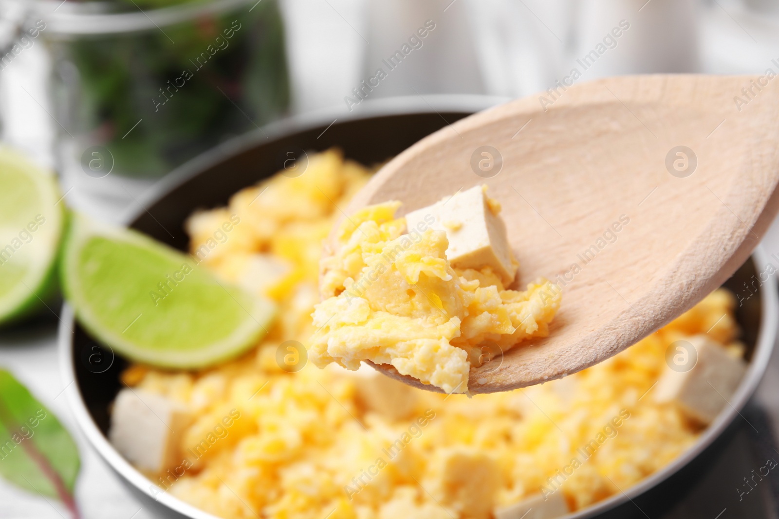 Photo of Taking delicious scrambled eggs and tofu with spoon from frying pan, closeup