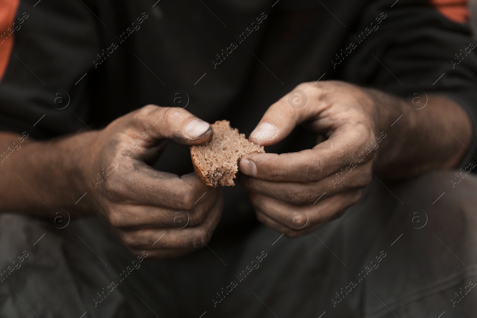 Photo of Poor homeless with piece of bread outdoors, closeup