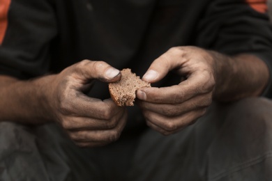 Poor homeless with piece of bread outdoors, closeup