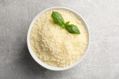 Bowl with grated parmesan cheese and basil on grey table, top view