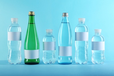 Different bottles of pure water with blank tags on color background