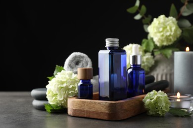 Spa composition. Cosmetic products, burning candles and hydrangea flowers on gray table against black background, space for text