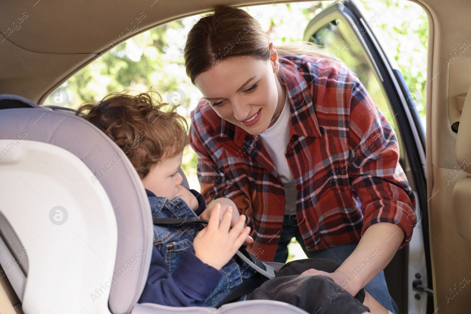 Photo of Mother fastening her son in child safety seat inside car