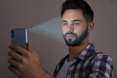 Young man unlocking smartphone with facial scanner on beige background. Biometric verification