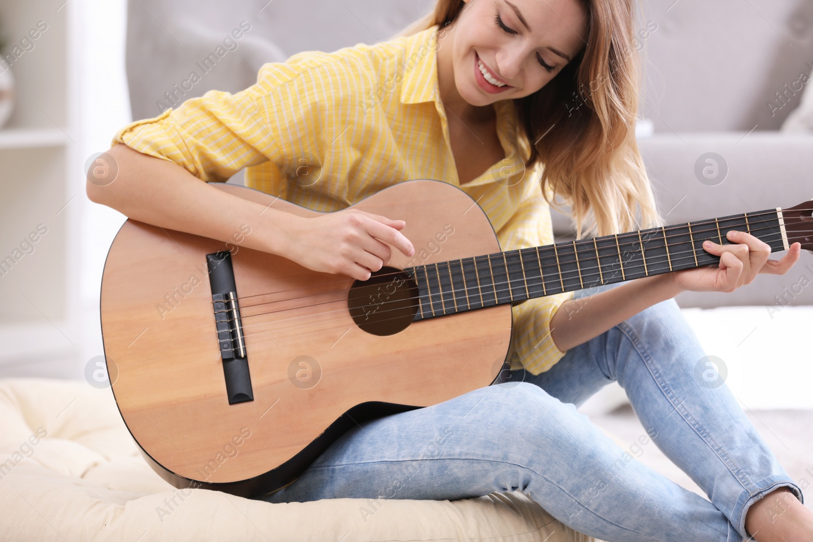 Photo of Young woman playing acoustic guitar at home