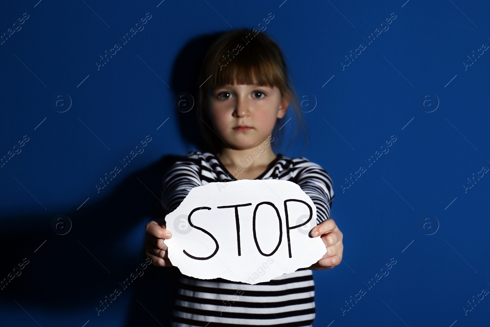 Photo of Abused little girl with sign STOP near blue wall. Domestic violence concept