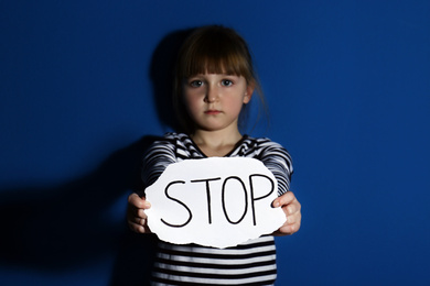 Abused little girl with sign STOP near blue wall. Domestic violence concept