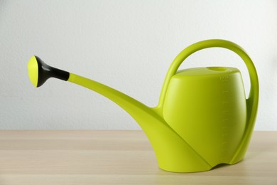 Green plastic watering can on wooden table against white background