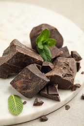 Photo of Tasty dark chocolate pieces with mint on white board, closeup