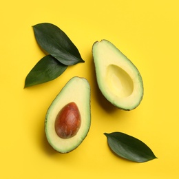 Photo of Cut ripe avocado and green leaves on yellow background, flat lay