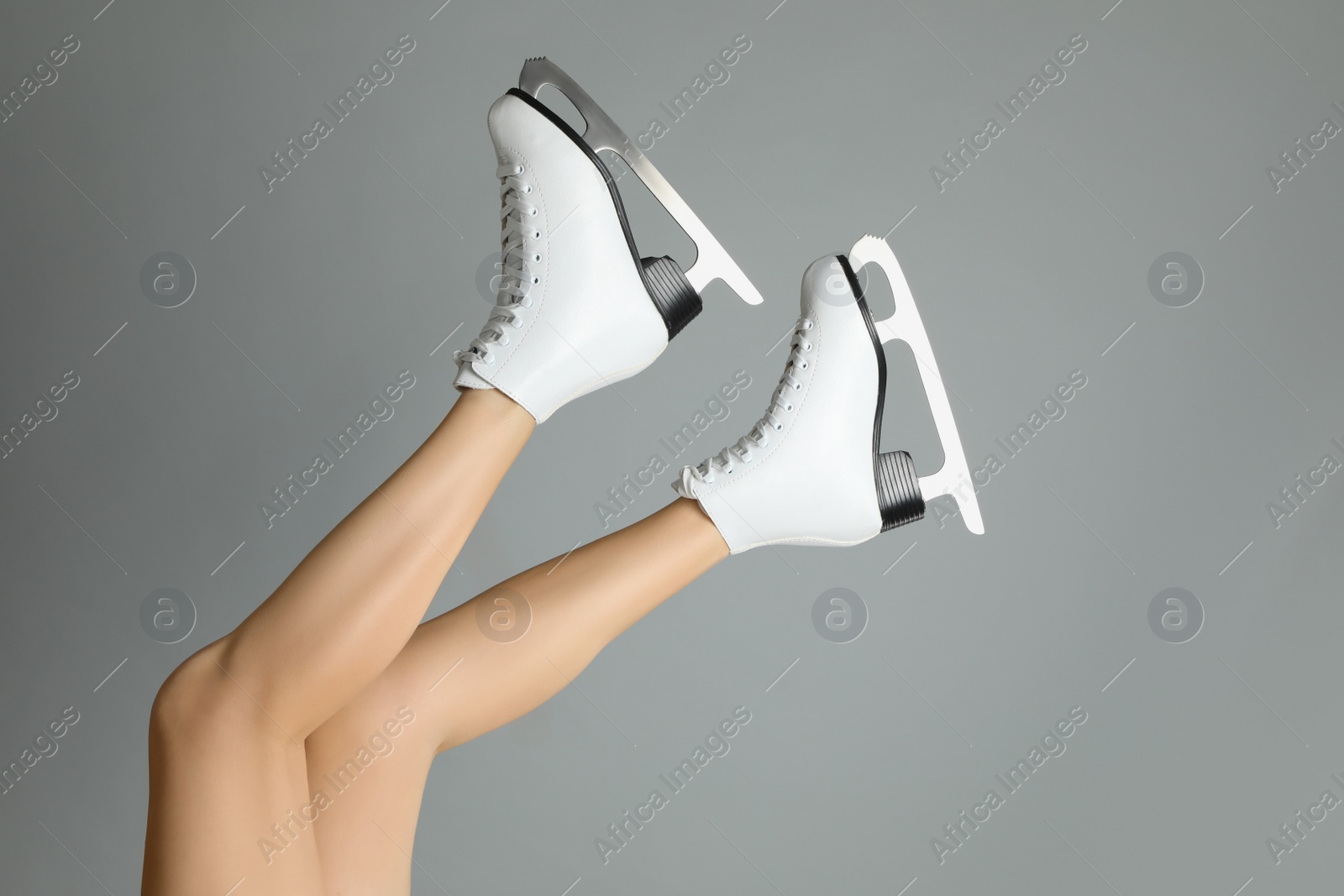 Photo of Woman in elegant white ice skates on grey background, closeup of legs