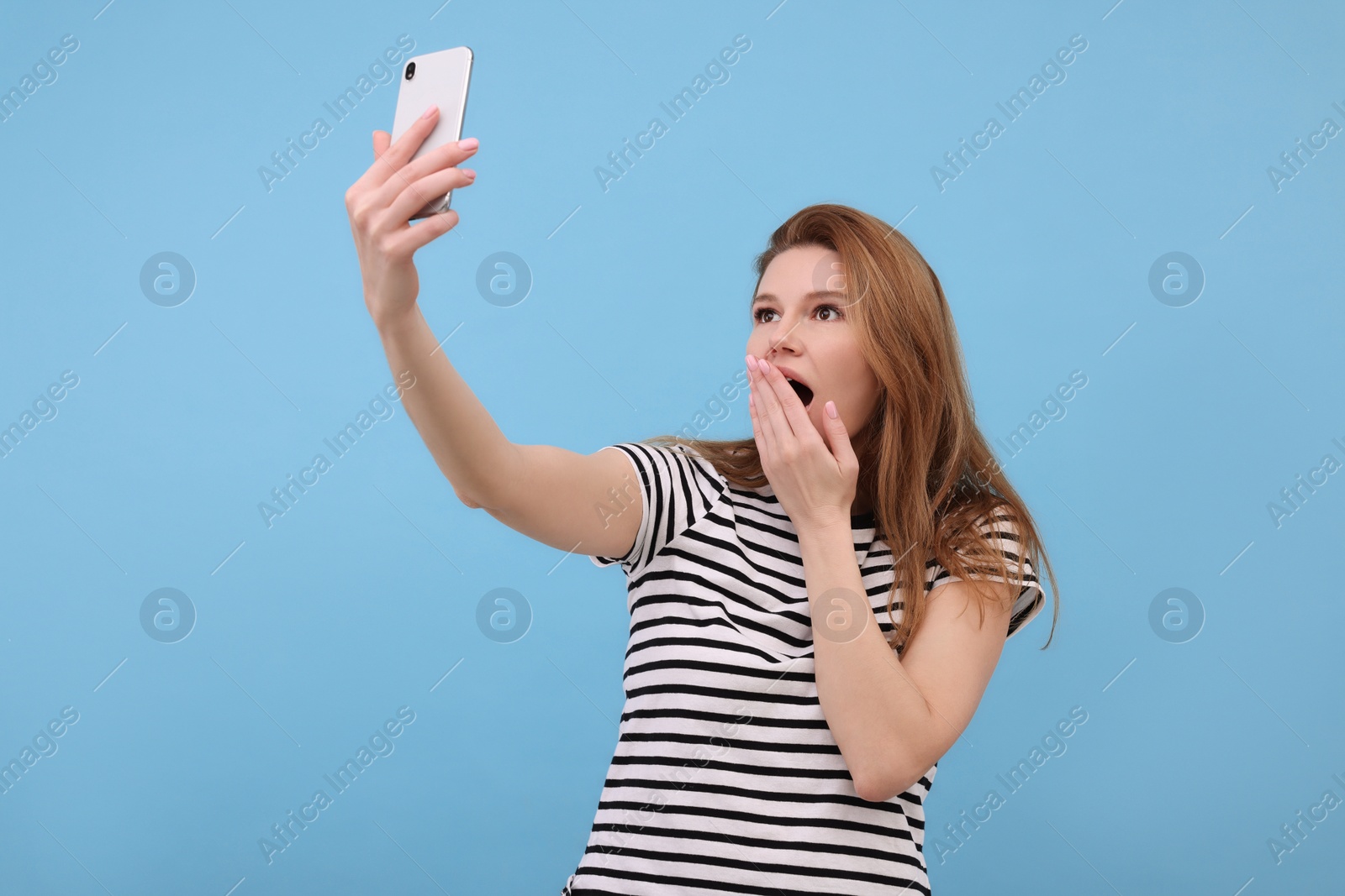 Photo of Shocked woman taking selfie on light blue background