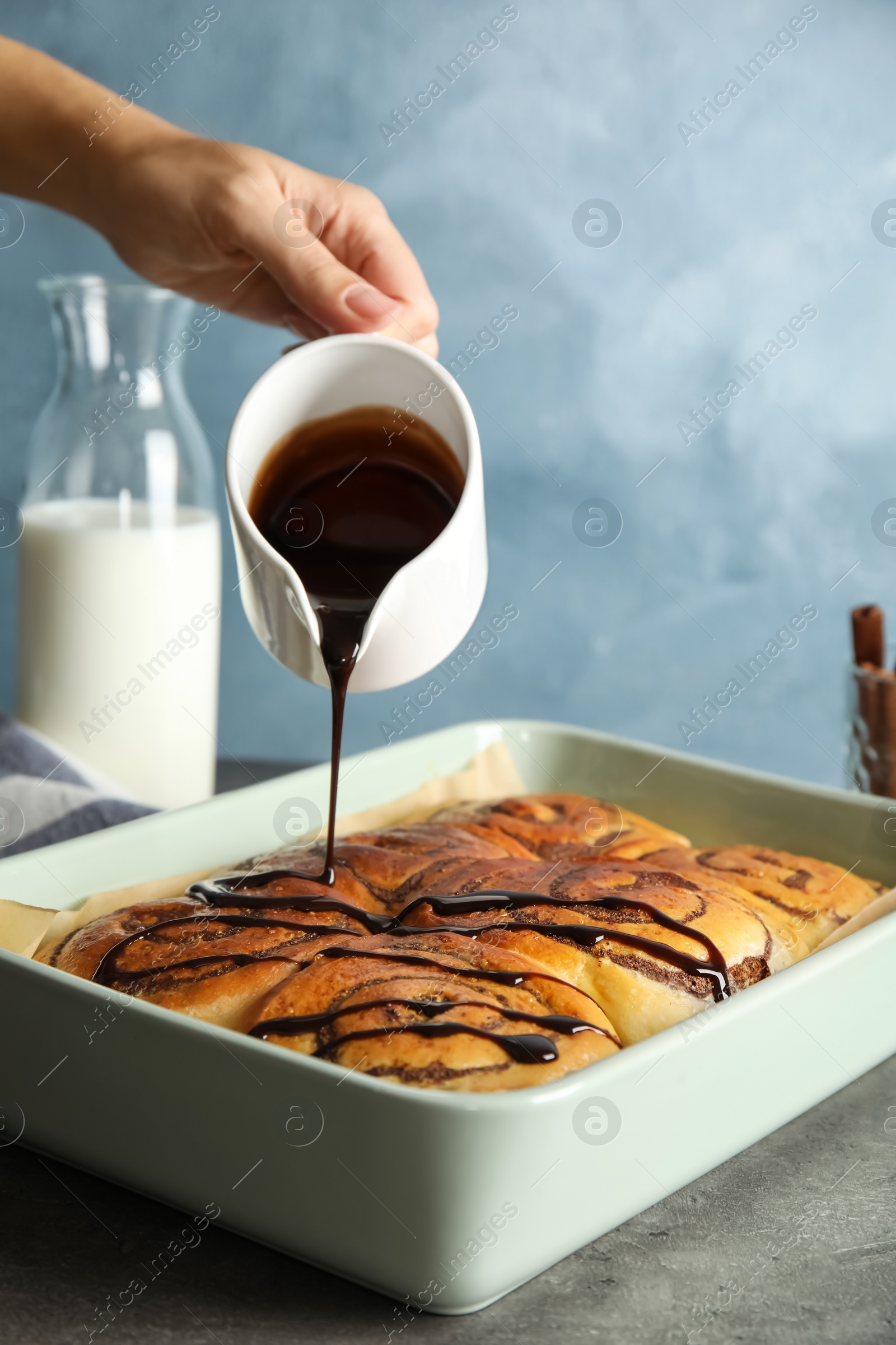 Photo of Woman pouring chocolate syrup onto freshly baked cinnamon rolls on table, closeup