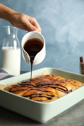 Woman pouring chocolate syrup onto freshly baked cinnamon rolls on table, closeup