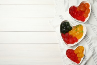 Photo of Delicious gummy fruit shaped candies on white wooden table, flat lay. Space for text