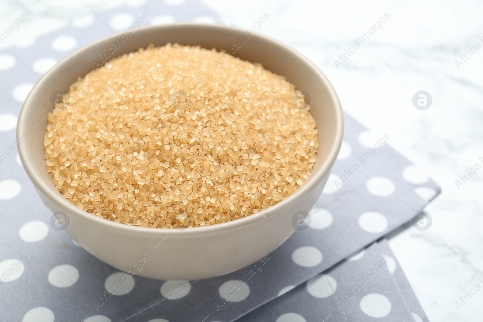 Photo of Brown sugar in bowl on white marble table, closeup. Space for text