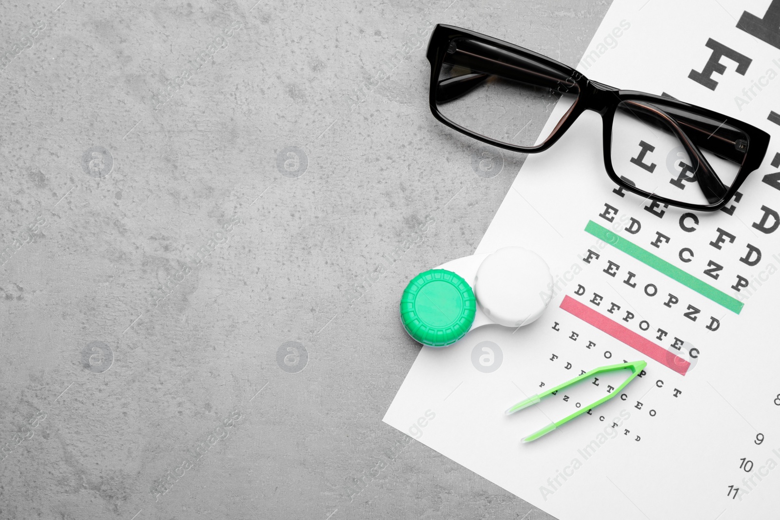 Photo of Case with contact lenses, tweezers, glasses and eye chart test on grey table, top view. Space for text