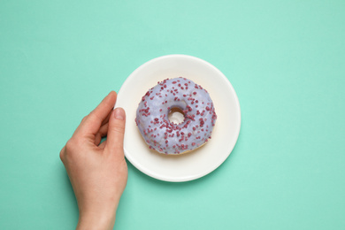 Photo of Woman holding plate with delicious glazed donut on turquoise background, top view