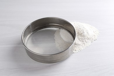 Photo of Metal sieve and flour on white wooden table
