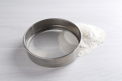 Metal sieve and flour on white wooden table