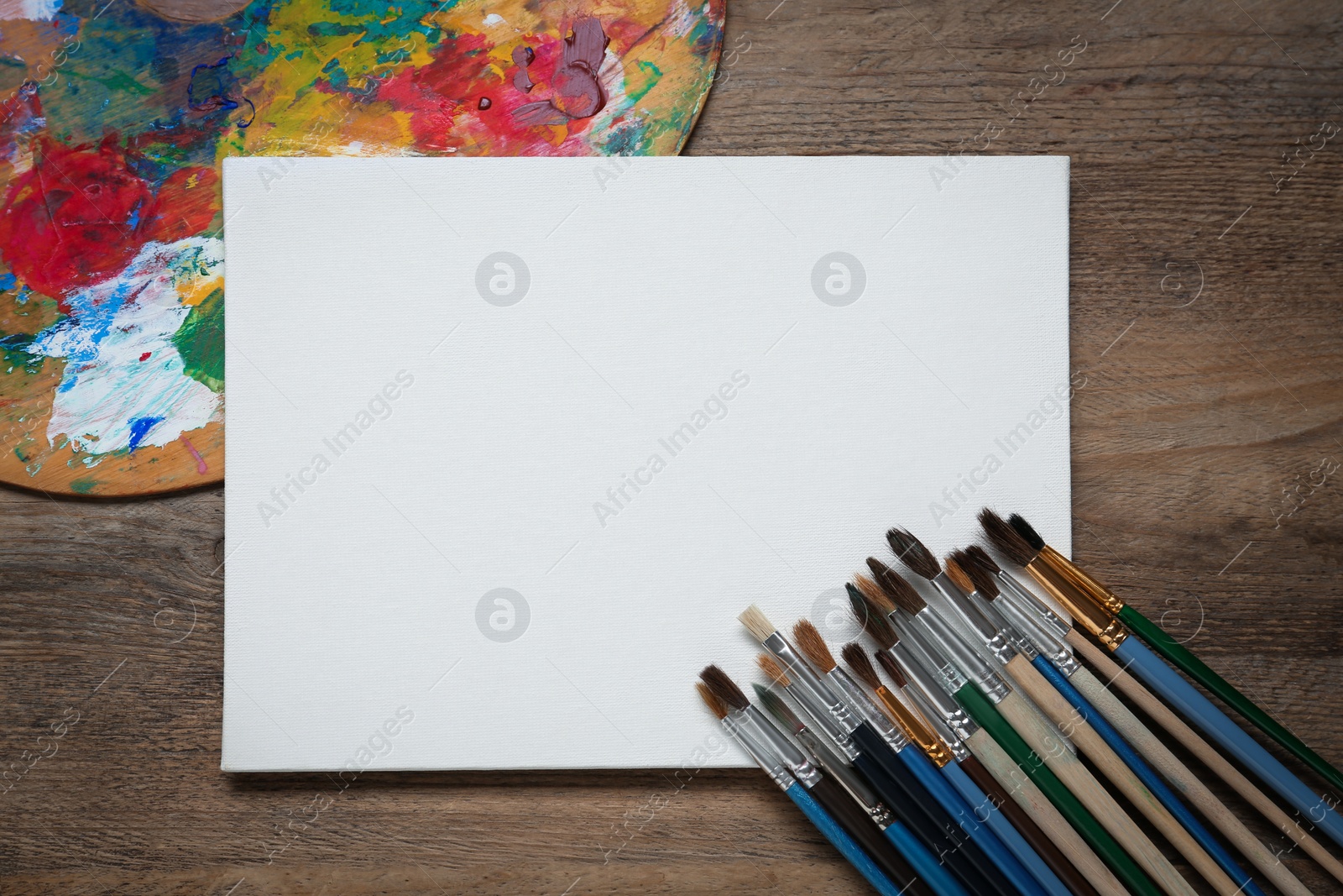 Photo of Blank canvas, brushes and palette on wooden table, flat lay. Space for text