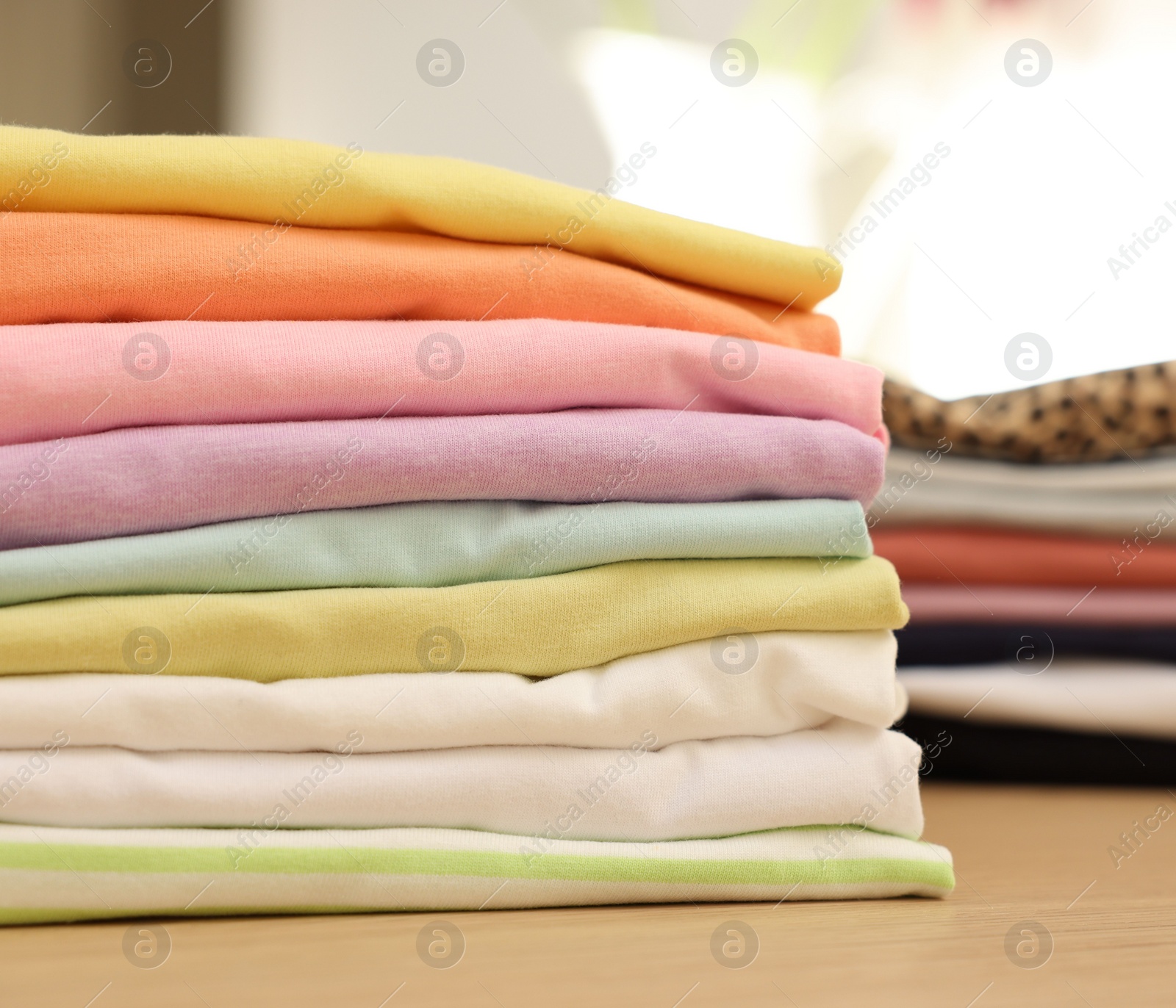 Photo of Many stacked clean clothes on wooden table, closeup