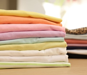 Many stacked clean clothes on wooden table, closeup