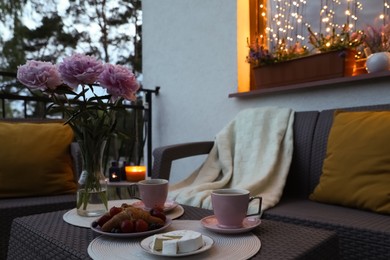 Photo of Rattan table with drink, food and flowers on outdoor terrace in evening