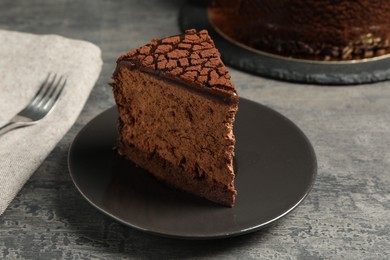 Photo of Piece of delicious chocolate truffle cake on grey textured table, closeup