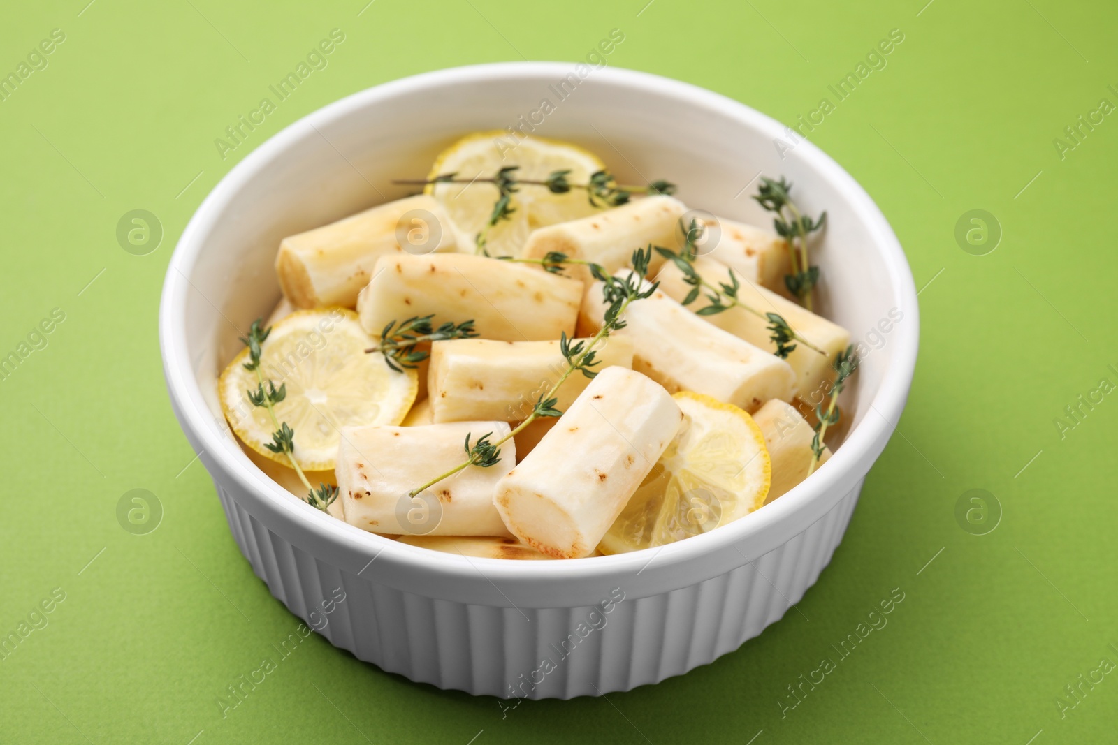 Photo of Dish with raw salsify roots, lemon and thyme on green table