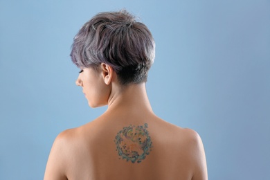 Photo of Beautiful tattoo on female back against color background