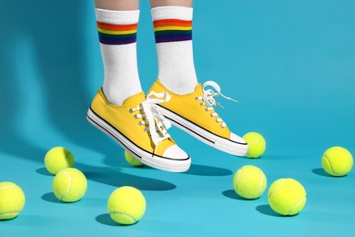 Woman in yellow classic old school sneakers jumping and tennis balls on light blue background, closeup