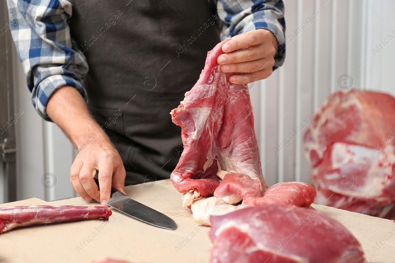 Photo of Butcher cutting fresh raw meat on counter in shop, closeup