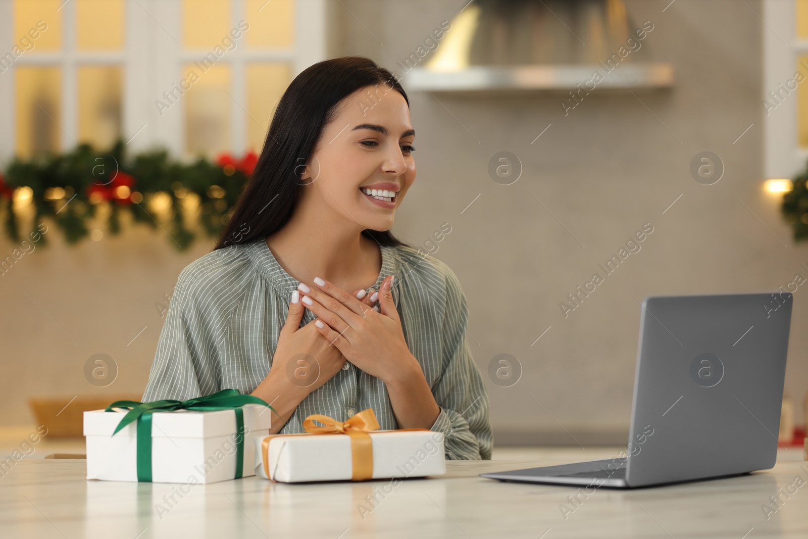 Photo of Celebrating Christmas online with exchanged by mail presents. Smiling woman thanking for gift during video call at home