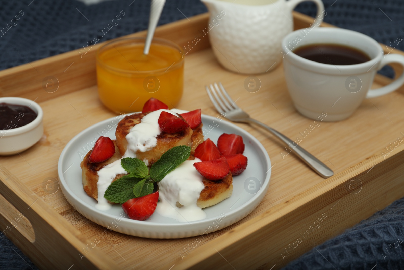 Photo of Delicious cottage cheese pancakes with fresh strawberries, sour cream and mint served on wooden tray, closeup