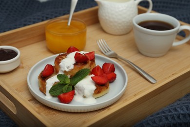 Photo of Delicious cottage cheese pancakes with fresh strawberries, sour cream and mint served on wooden tray, closeup
