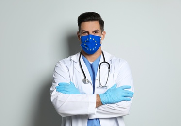 Doctor wearing medical mask with European Union flag on light background. Coronavirus outbreak in Europe