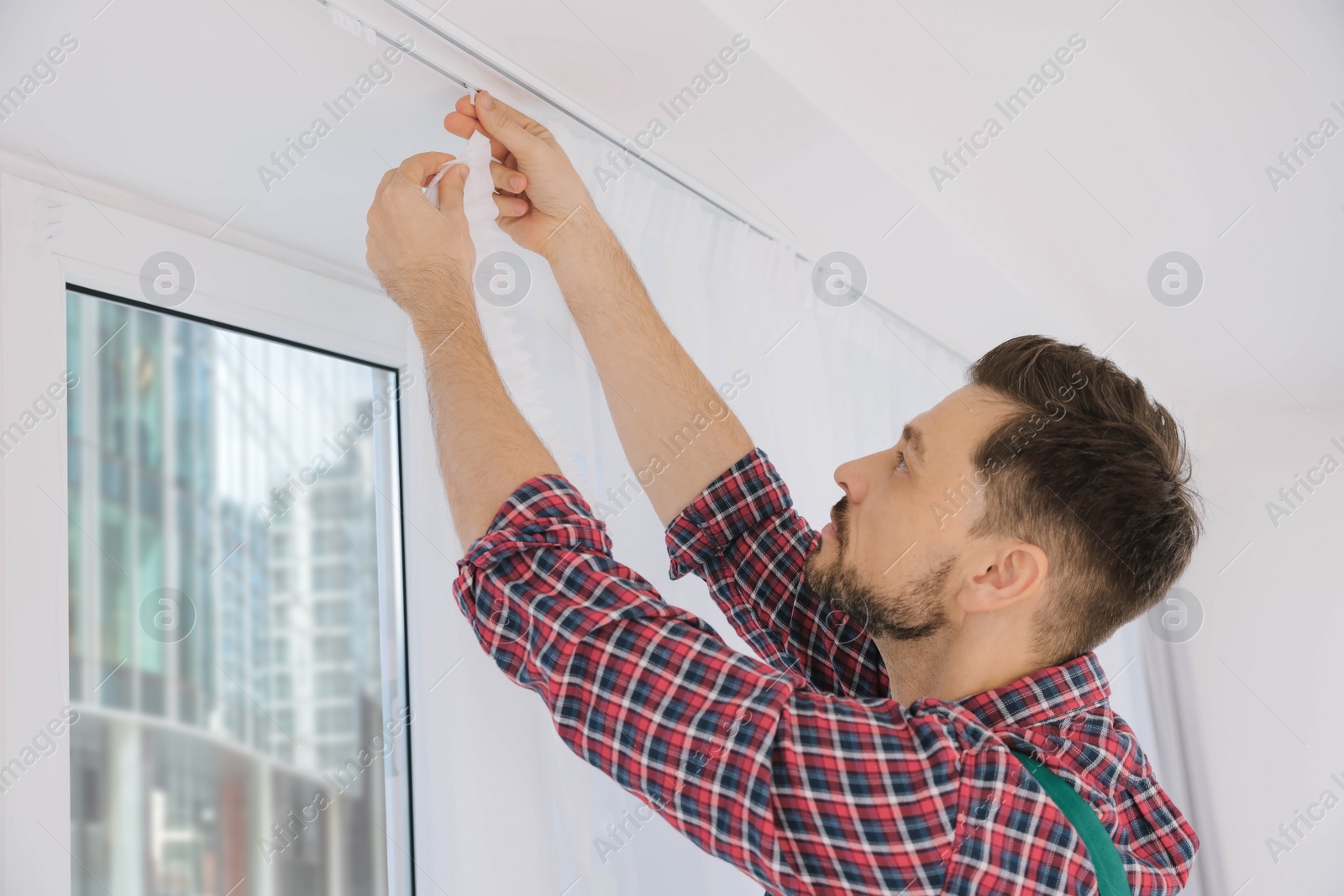 Photo of Worker in uniform hanging window curtain indoors, low angle view