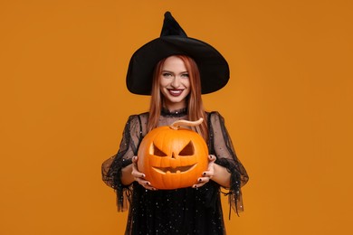 Photo of Happy young woman in scary witch costume with carved pumpkin on orange background. Halloween celebration