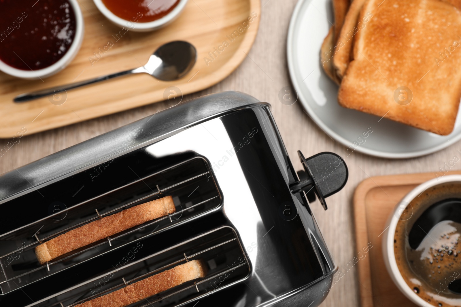 Photo of Toaster, roasted bread, jams and coffee on wooden table, flat lay