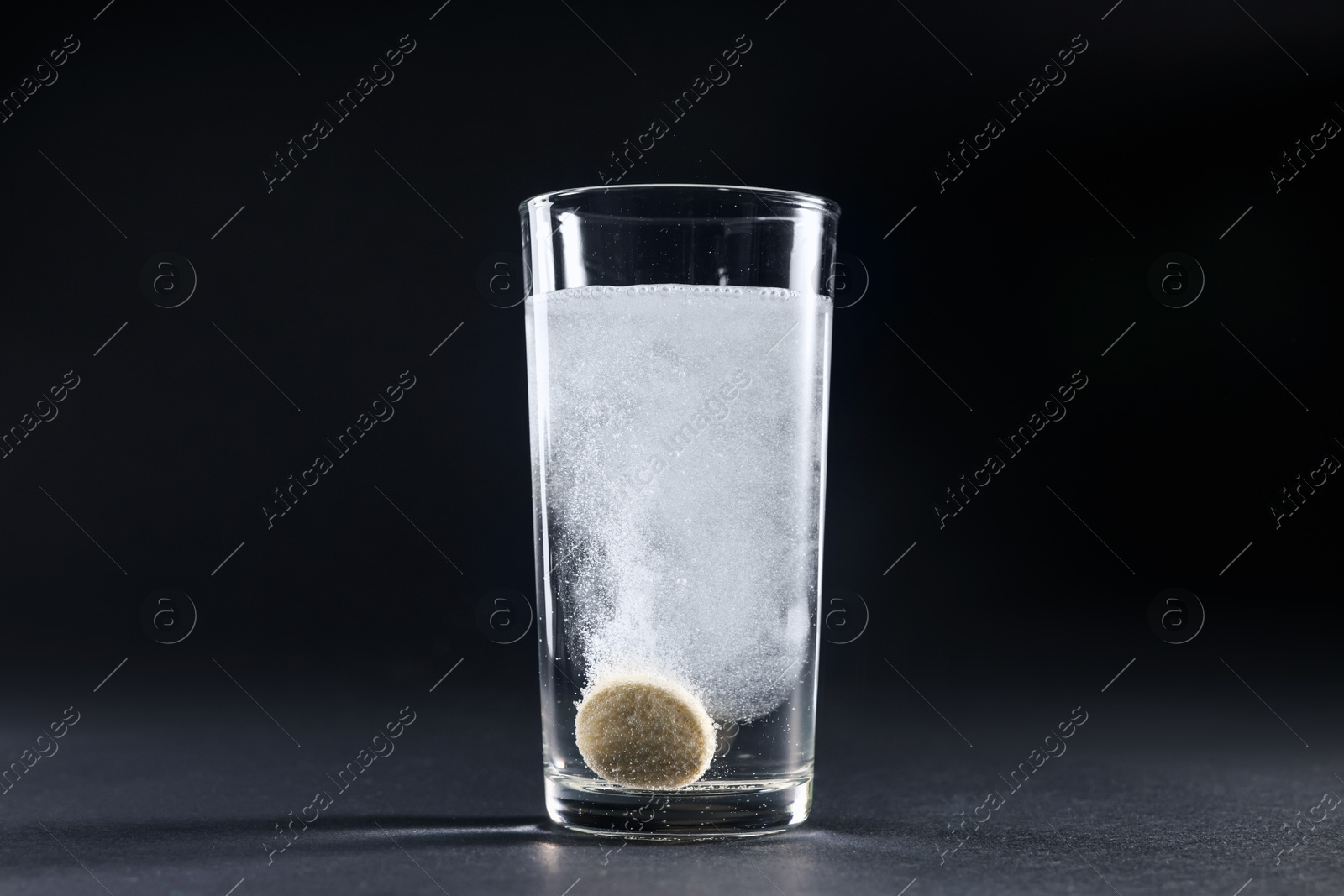 Photo of Effervescent pill dissolving in glass of water on grey table